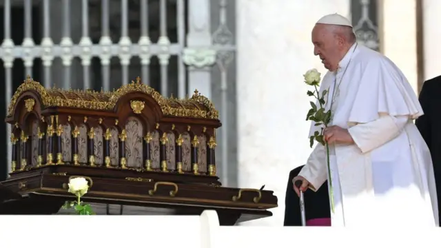 صورة للبابا فرنسيس يقف أمام صندوق يحتوي رفات القديسة تريز وفي يده وردة بيضاء 