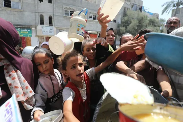 فلسطينيون يحملون الأواني وينتظرون الحصول على وجبة ساخنة توزعها جمعية خيرية  في مخيم النصيرات للاجئين في دير البلح، في ظل هجمات وحصار الجيش الإسرائيلي.